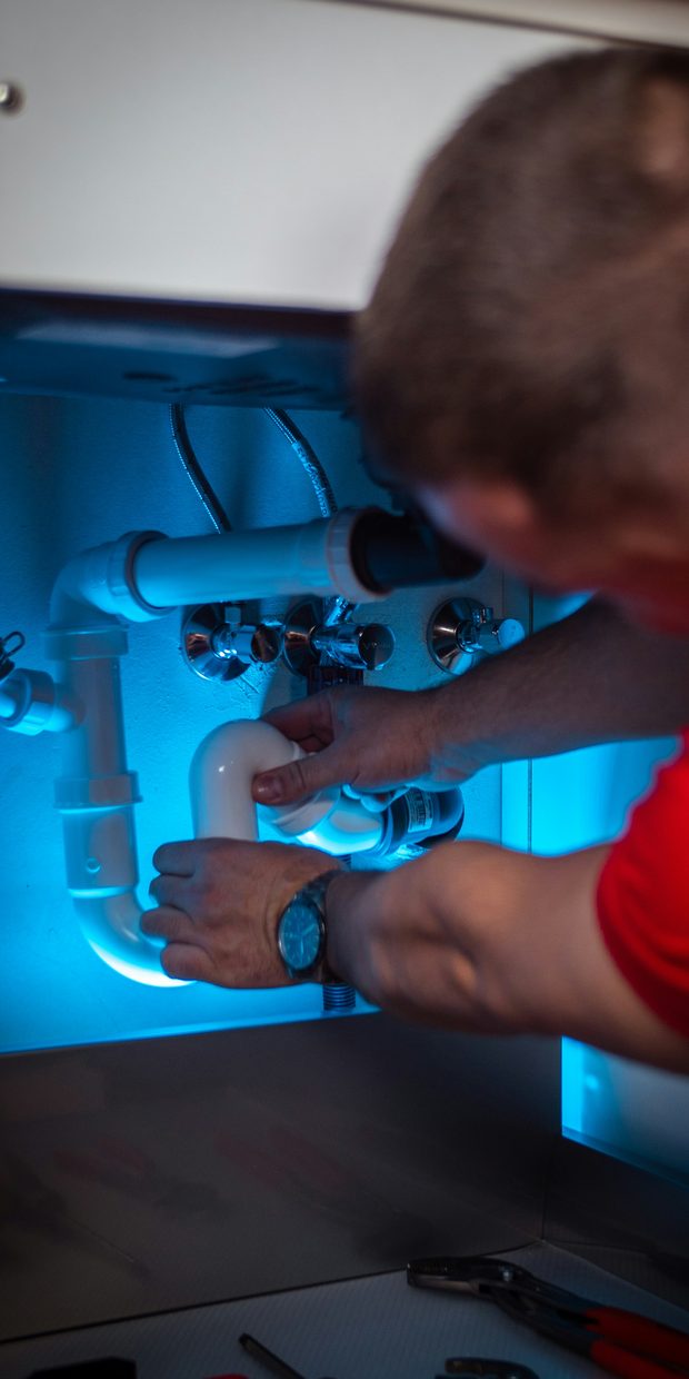 Plumber working on pipework under a sink